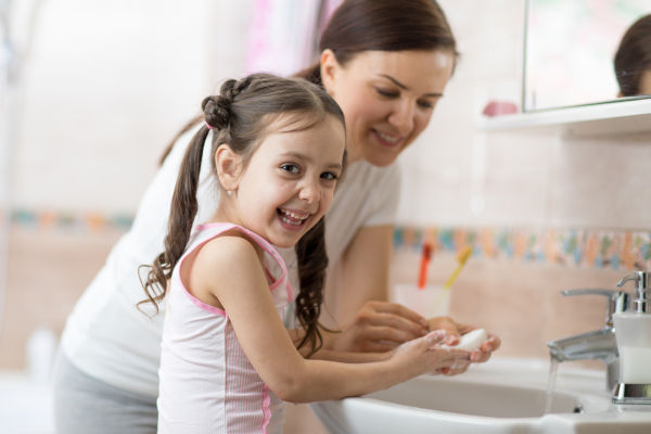 Woman and her daughter child washing hands with soap in bathroom