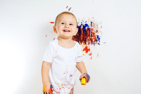Young child spreading multi coloured paint on house wall