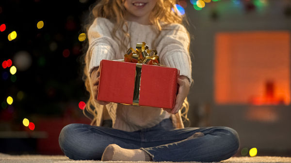 Little girl holding out Xmas present to camera, charity on Christmas benevolence